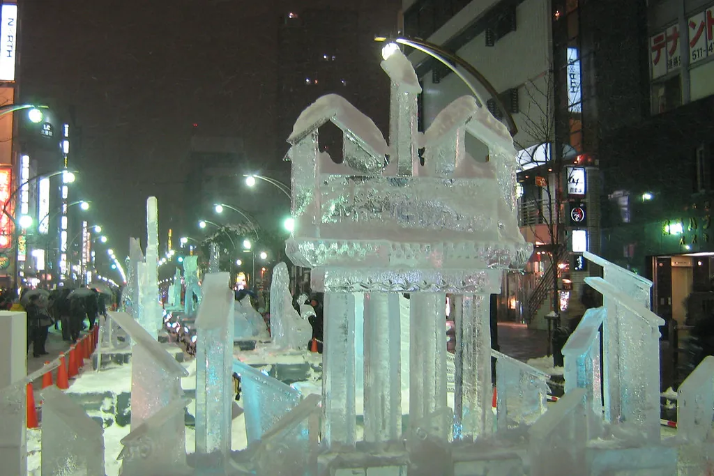 A row of illuminated ice sculptures lining a snowy street in Susukino at night, with shop signs in the background