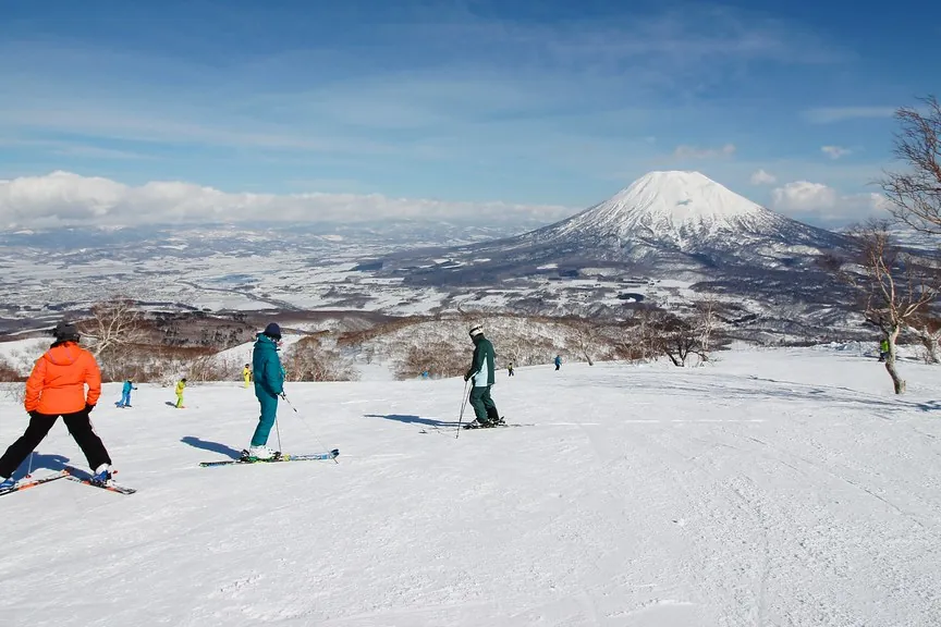 Niseko Grand Hirafu의 눈 덮인 슬로프를 내려가는 스키어들과 뒤편의 눈 덮인 요테이산