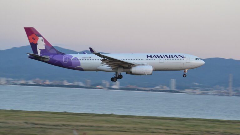 A Hawaiian Airlines Airbus A330 with purple tail livery descending low over water, landing gear down, near Kansai Internation