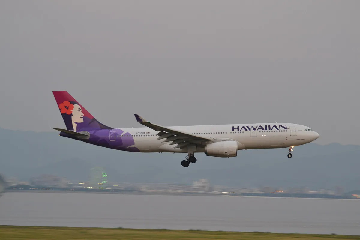A Hawaiian Airlines Airbus A330 with purple tail livery on final approach over water, landing gear down, near Kansai Internat