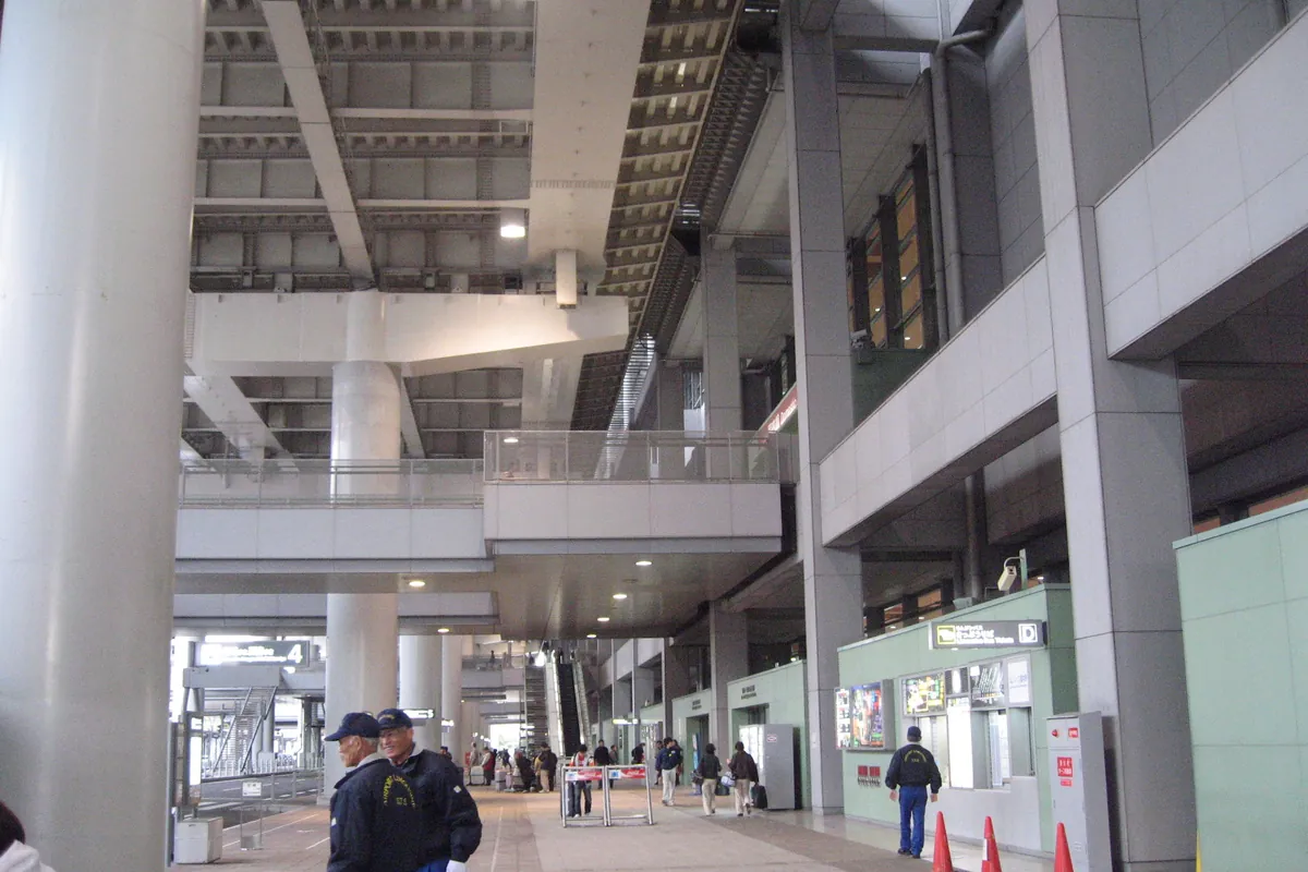 Interior hall of a Kansai International Airport terminal building with concrete pillars, escalators, and people walking throu