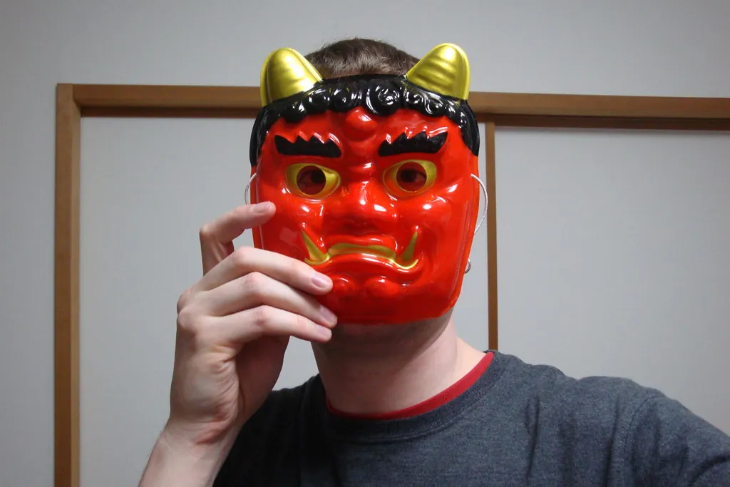 有人举在脸前的红色鬼面具，带金色犄角和黑色头发