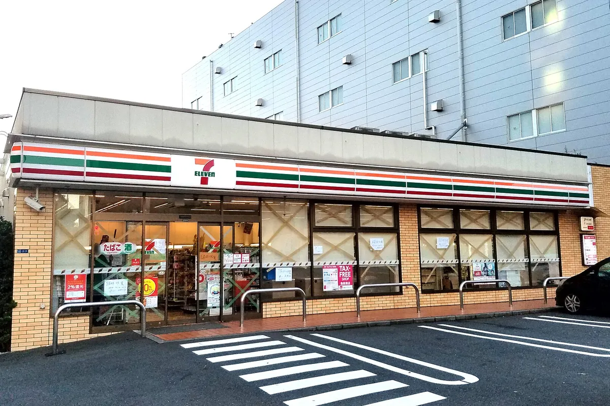 Exterior of a 7-Eleven convenience store with a striped awning and a car parked in front
