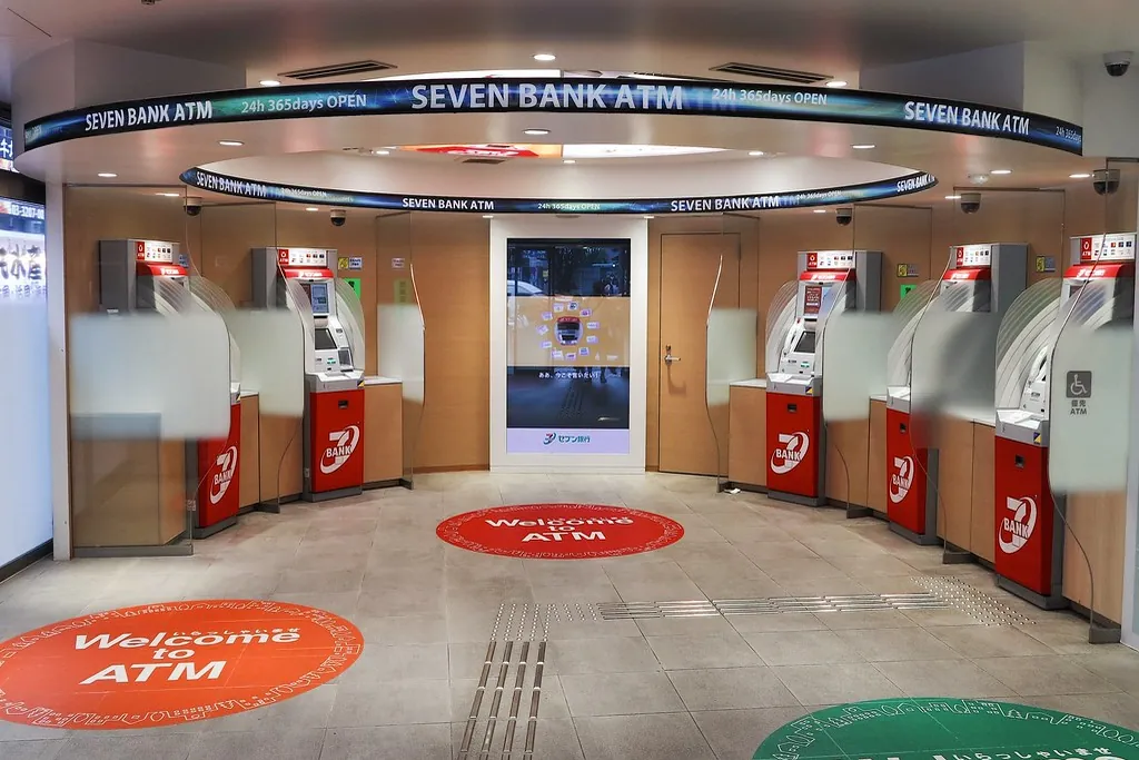 Curved row of Seven Bank ATM machines under a SEVEN BANK ATM sign, with red floor decals reading Welcome to ATM