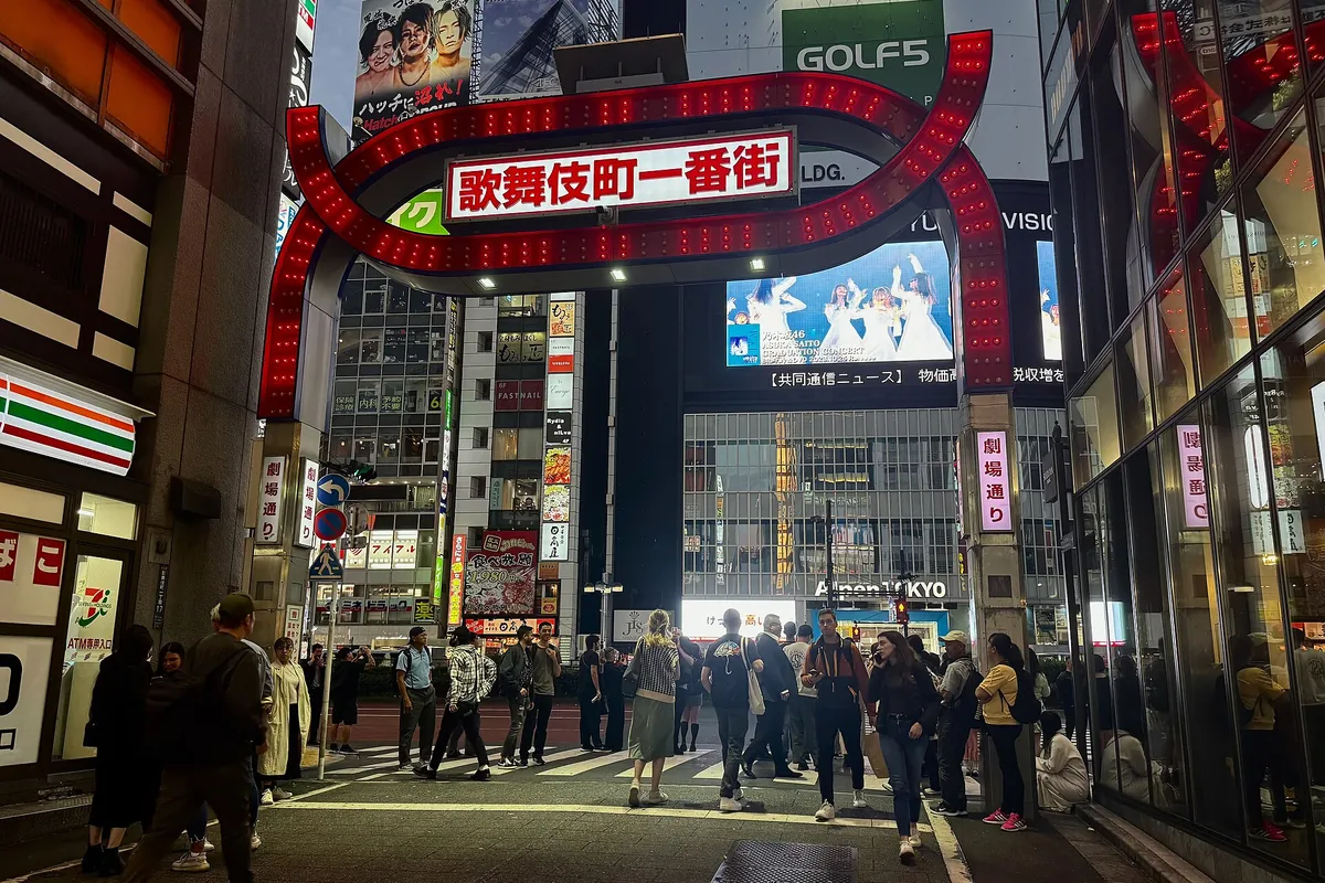 The red neon Kabukicho Ichiban-gai gate lit up at night above a busy street with pedestrians in Shinjuku, Tokyo