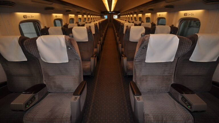 Rows of brown two-by-two reclining seats with white headrest covers inside a Shinkansen Green Car