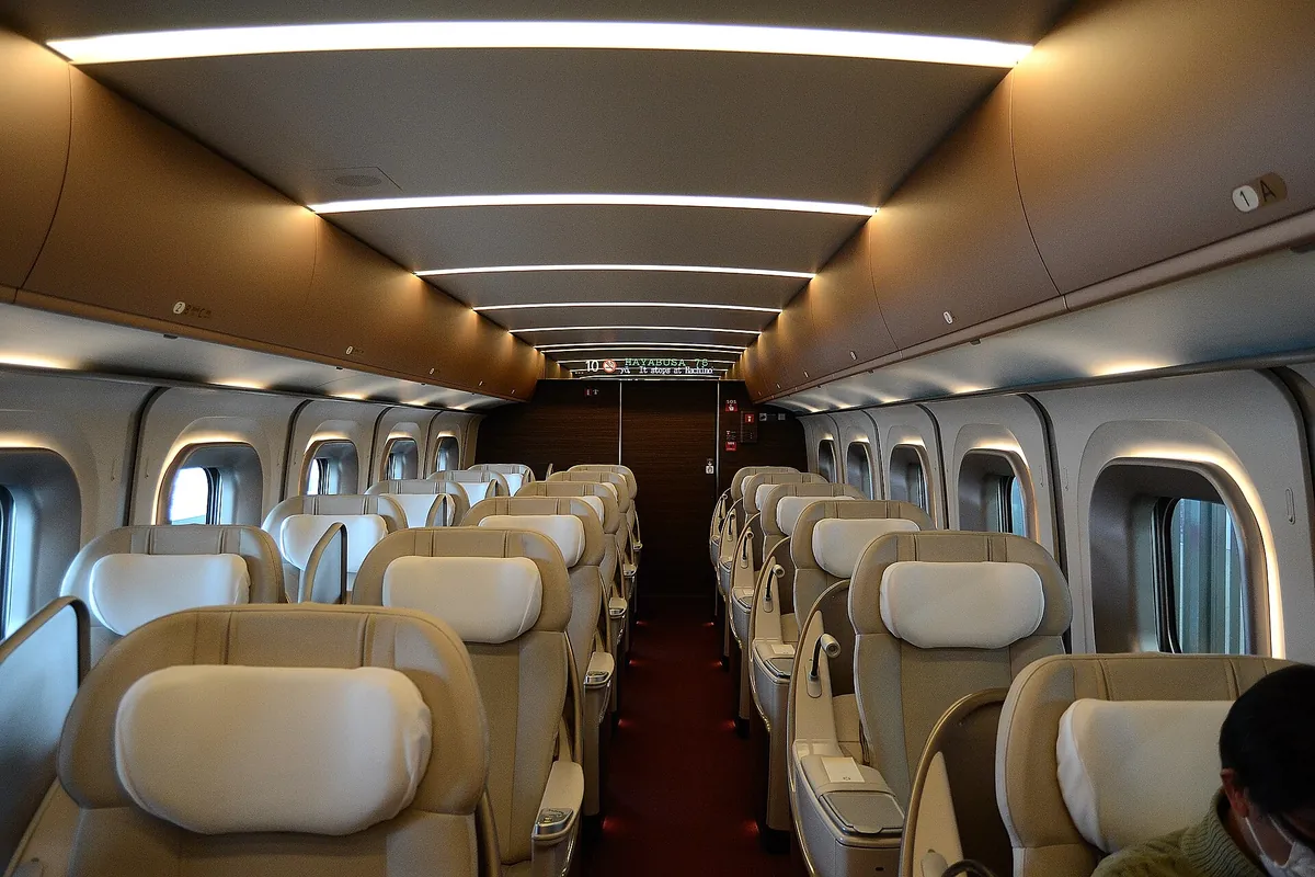Interior of a Shinkansen GranClass cabin with rows of cream leather reclining seats arranged two by two