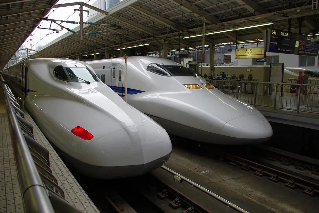 Two differently shaped Shinkansen trains parked nose to nose at a station platform, with a Tokyo station sign visible