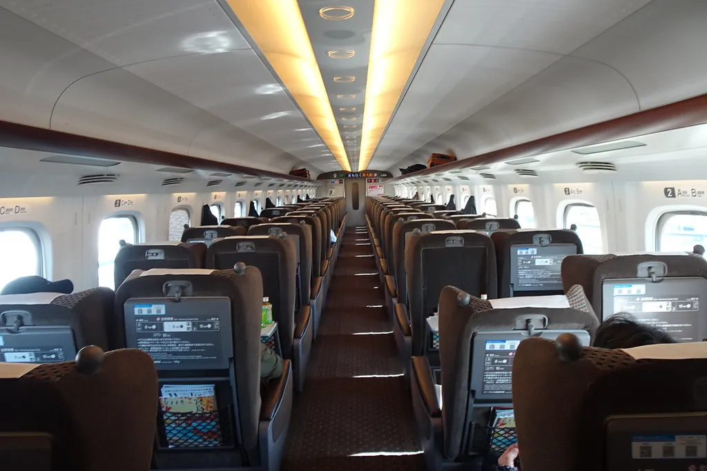 Interior of a Shinkansen Green Car with rows of reclining seats, headrests, and a center aisle