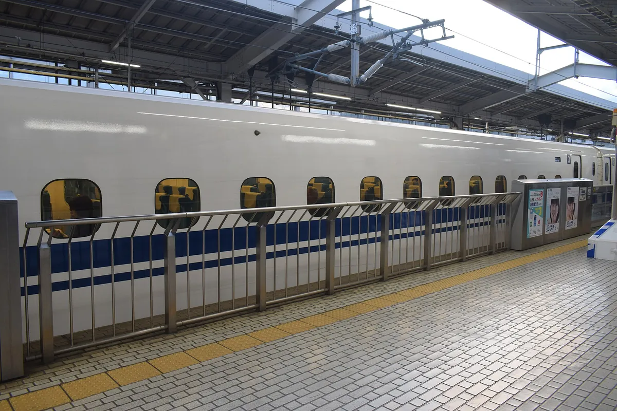 停靠在JR京都站站台的白色蓝条纹东海道新干线列车侧面，前方有护栏