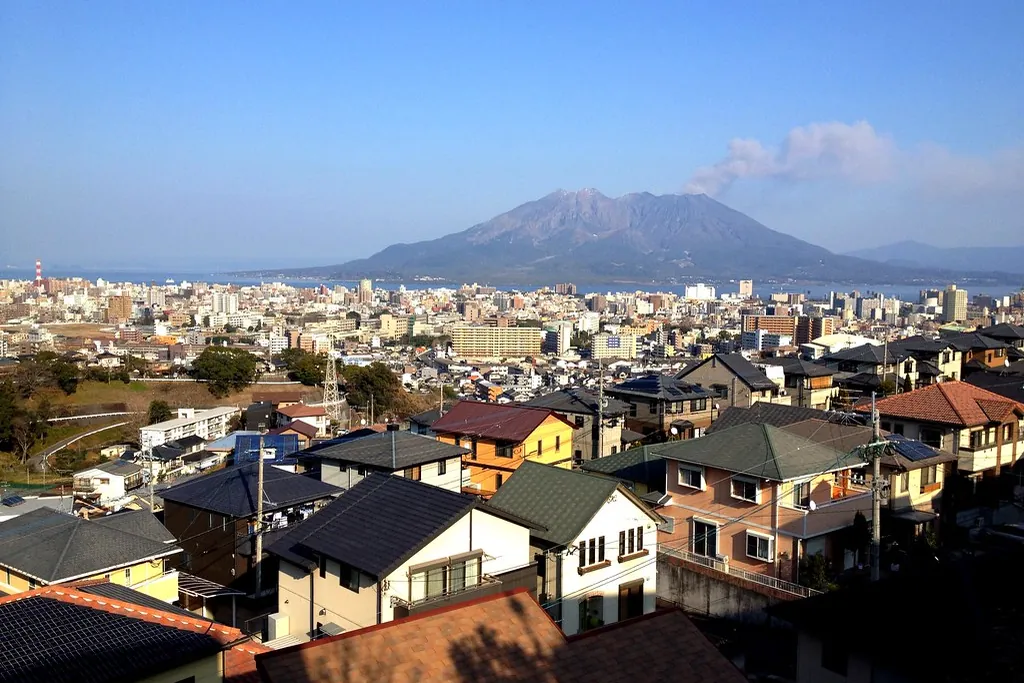 隔着海湾冒烟的樱岛火山，前景是鹿儿岛山坡上的房屋
