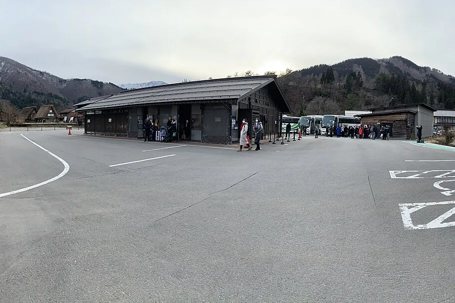앞마당에 버스와 승객이 있고 뒤로 산이 보이는 시라카와고 버스 터미널 건물