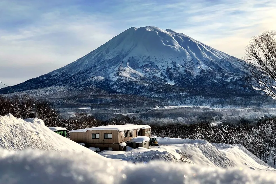 Snow-covered Mount Yotei volcano rising above a cabin and trees near Niseko, Hokkaido