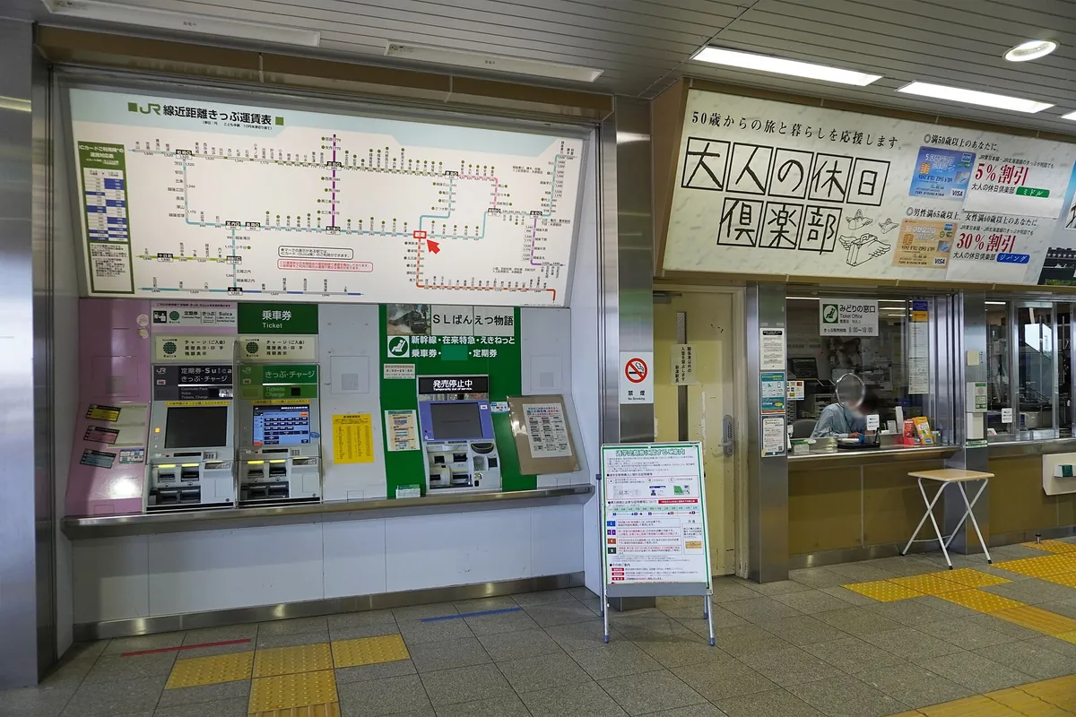 JR ticket vending machines and a fare map next to a staffed ticket counter inside Niitsu Station
