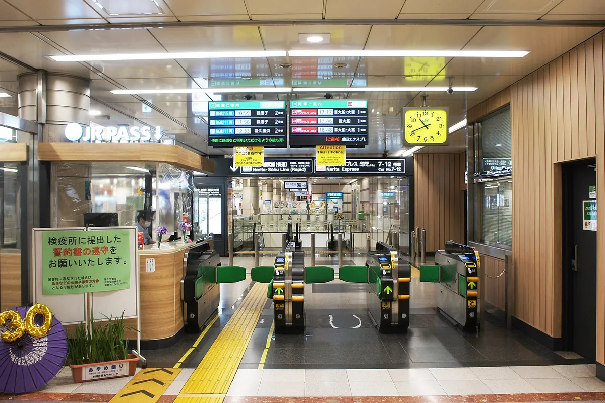 Green automatic ticket gates below train schedule boards at Narita Airport Terminal 1 Station