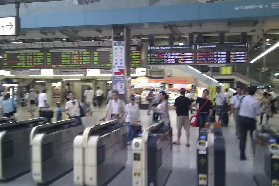 Travelers passing through ticket gates below a departure board at JR Ueno Station in Tokyo