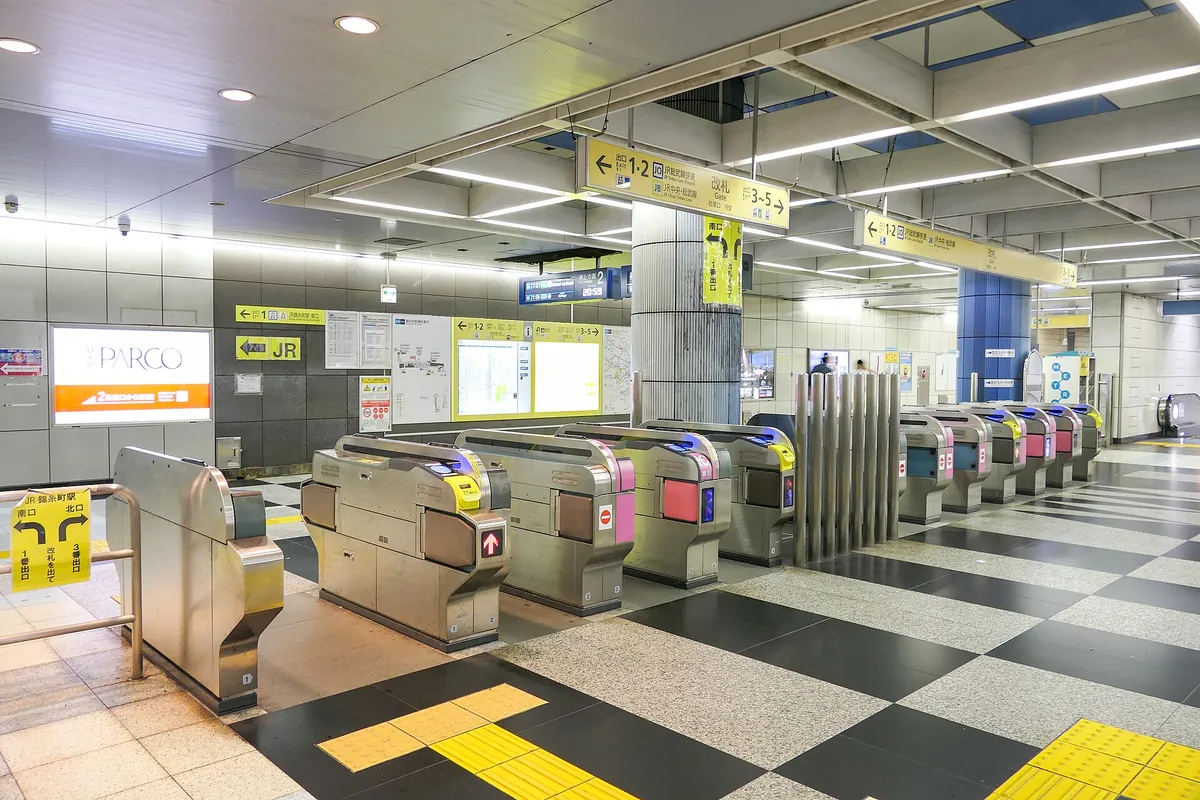 Automatic ticket gates below directional signs on a checkered floor at Kinshicho Station in Tokyo