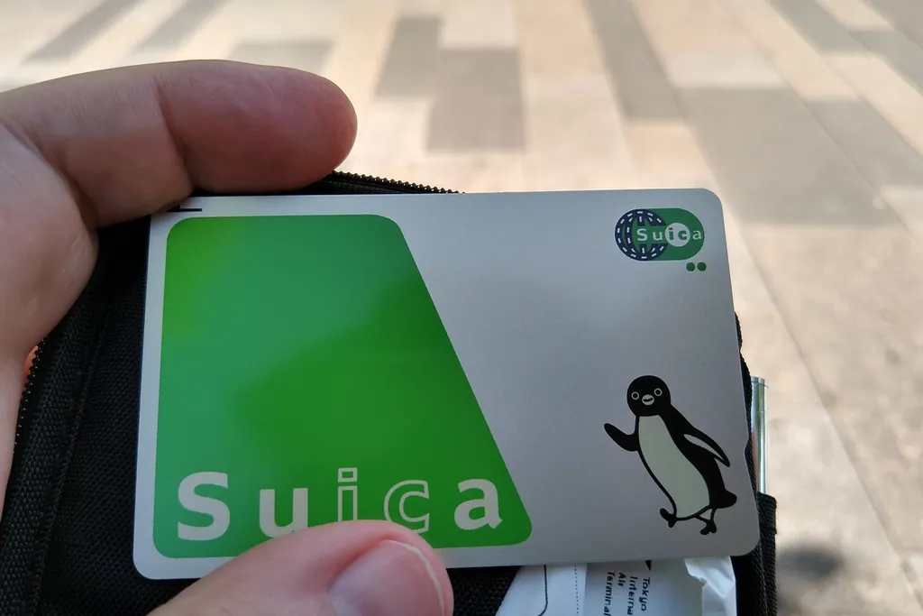 A hand holding a green Suica IC card with a penguin logo