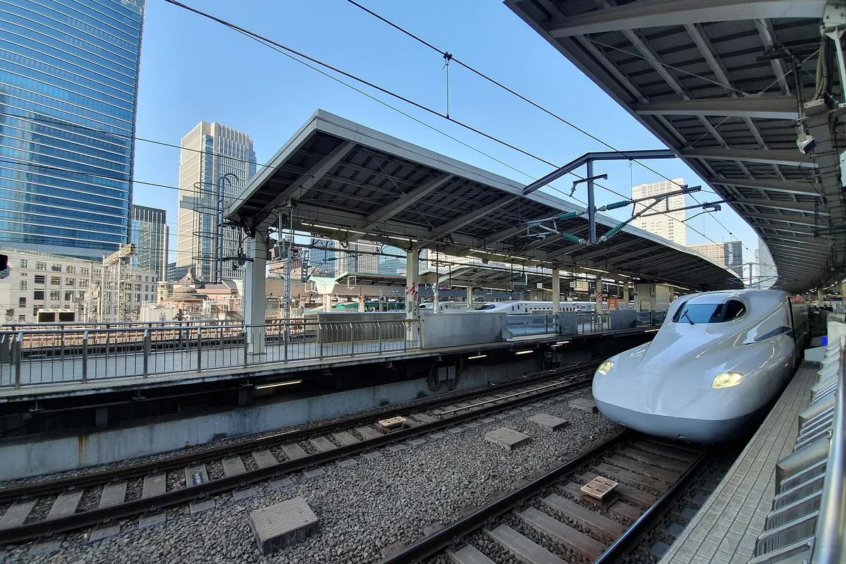 A Shinkansen train at a platform in Tokyo Station with the city skyline behind it