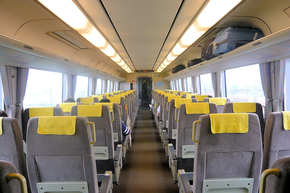 Rows of gray seats with yellow headrest covers inside a Japanese limited express train