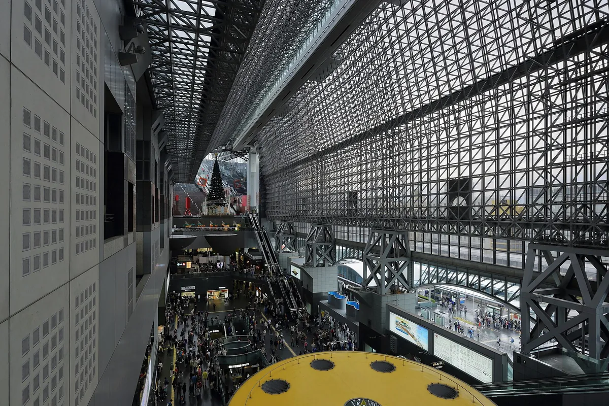 Tall atrium inside Kyoto Station with a lattice roof, escalators, and crowds below