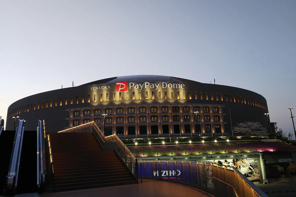 PayPay Dome stadium building in Fukuoka, Japan, lit up at dusk with escalators leading up to the entrance
