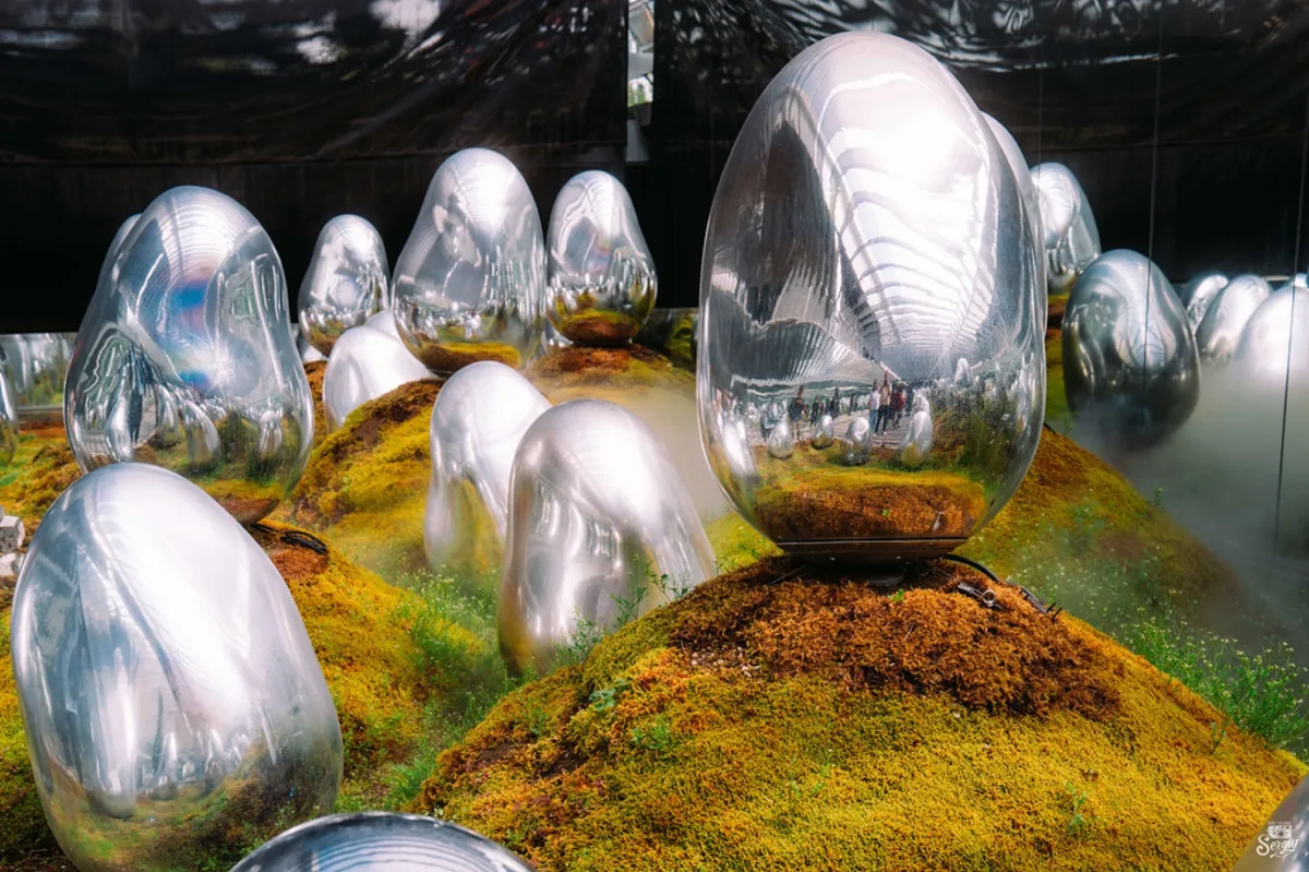 Mirrored egg-shaped sculptures on moss in the outdoor garden area
