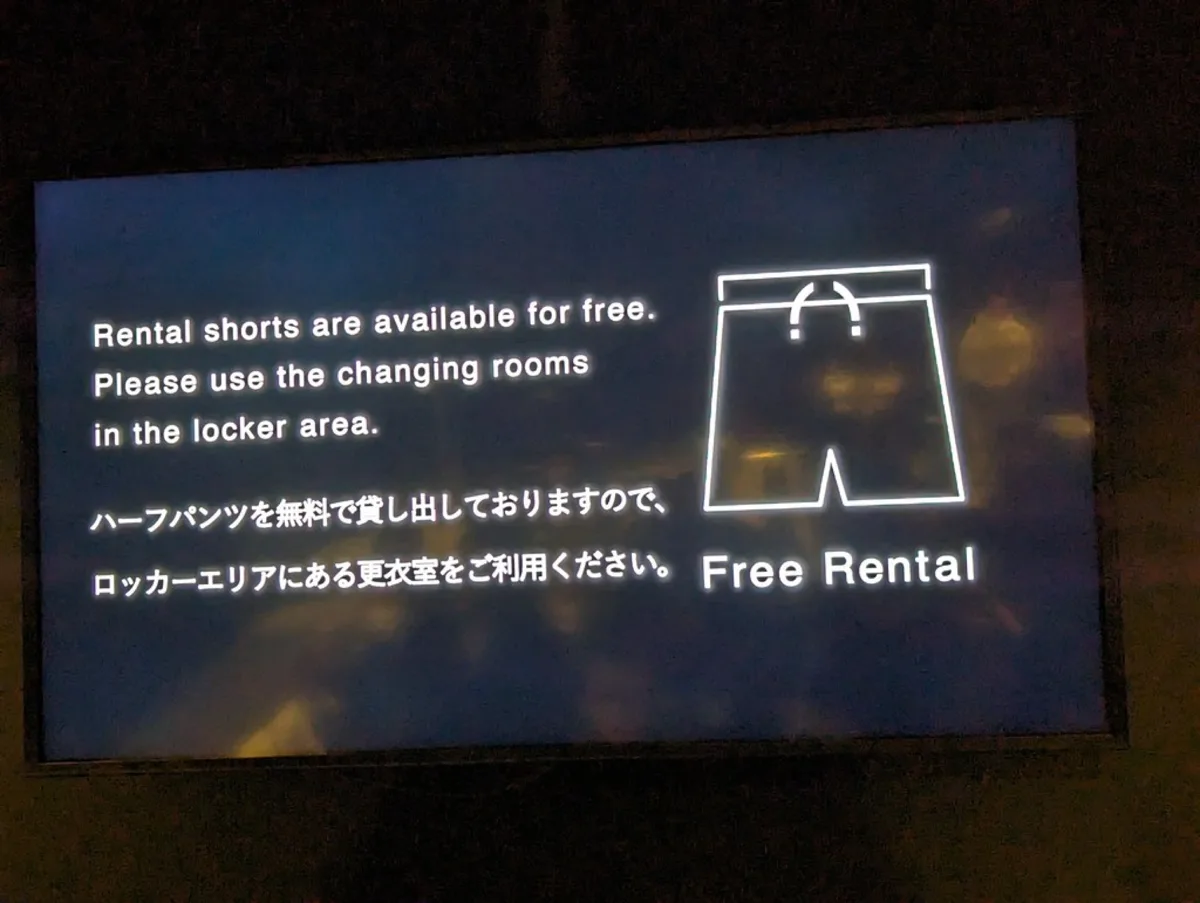 Bilingual sign saying free rental shorts and changing rooms are in the locker area