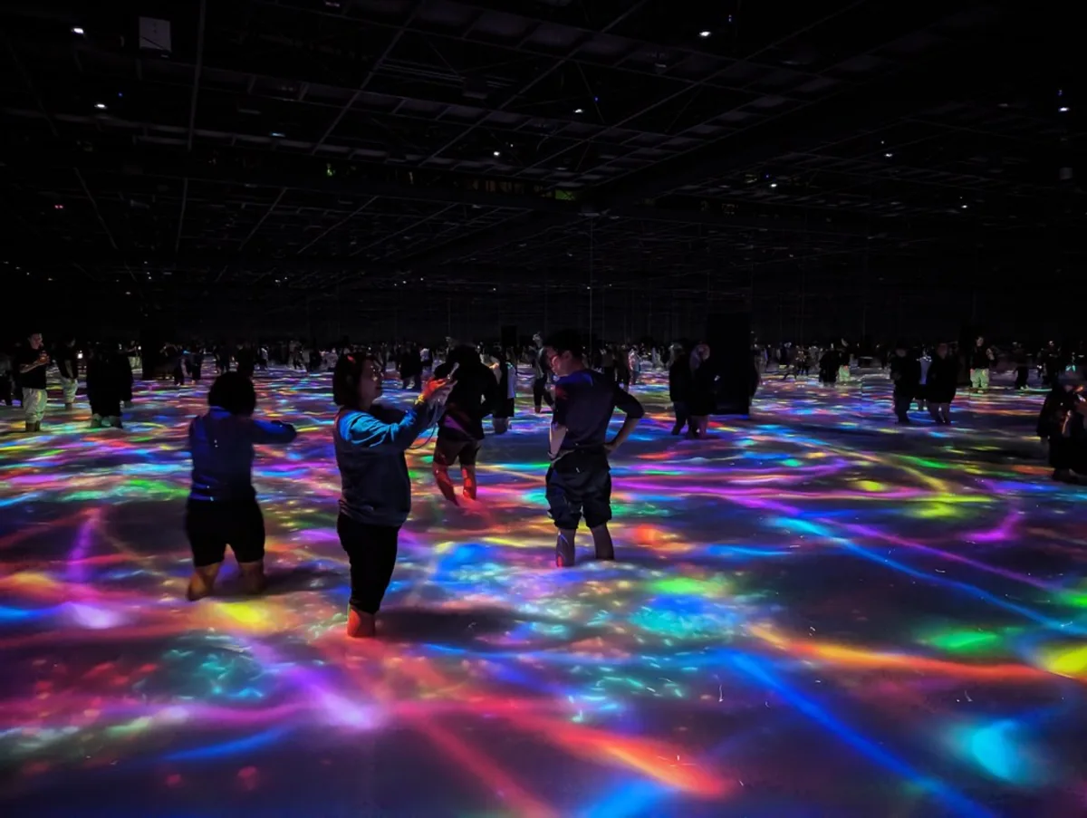 People wading knee-deep in a dark pool lit by colorful projections