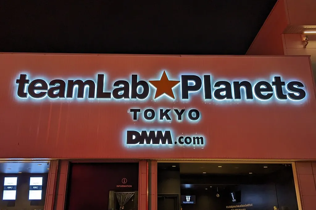 Illuminated teamLab Planets TOKYO sign with a DMM.com logo below it at night