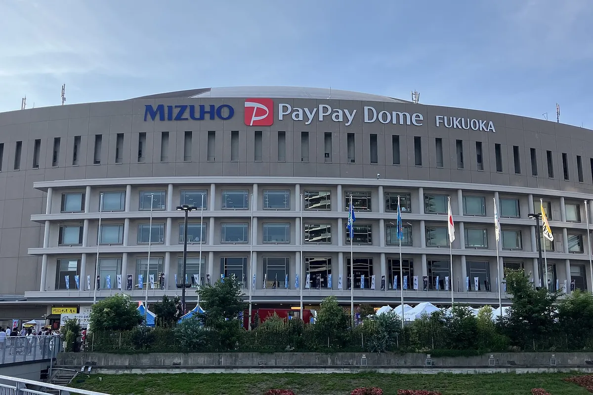 Exterior of the MIZUHO PayPay Dome Fukuoka stadium with its name on the facade and flags along the building