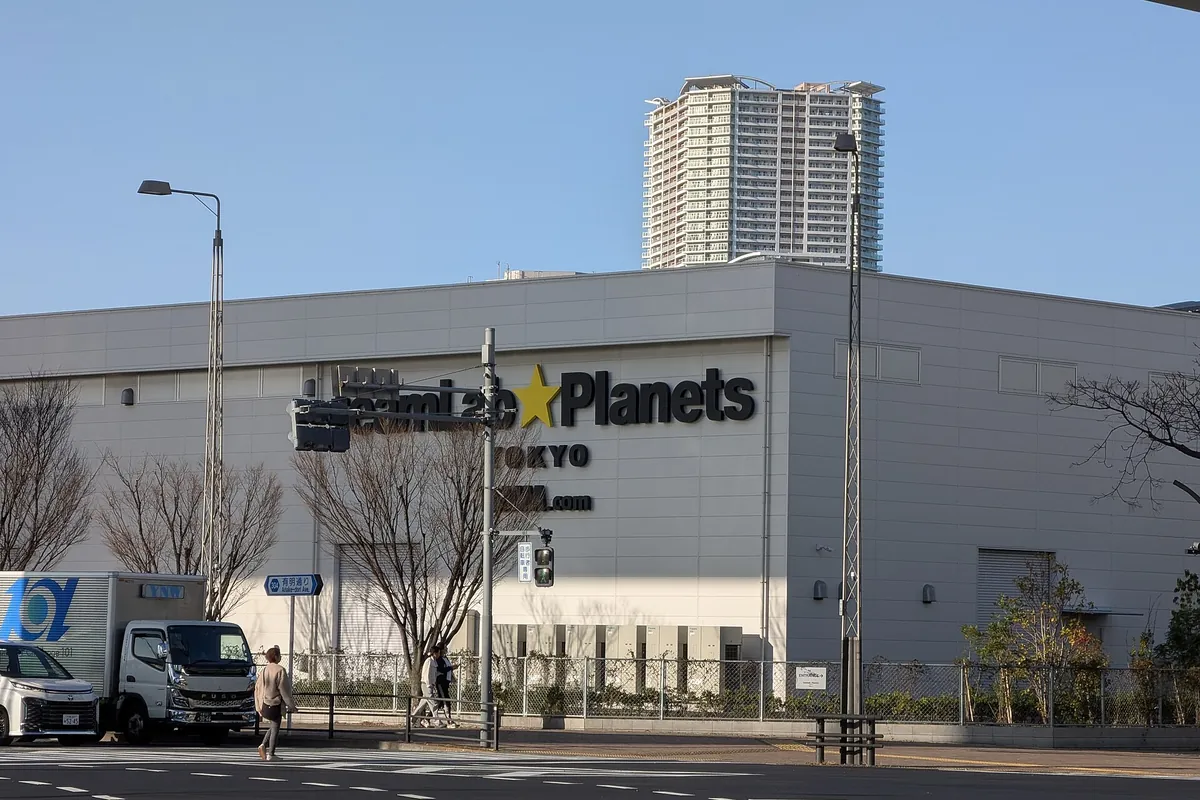 The teamLab Planets Tokyo building with its sign, seen from the street with a high-rise tower behind it