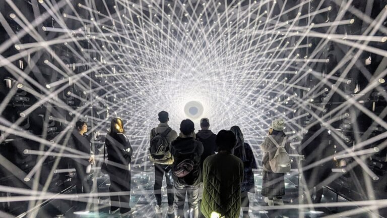 Visitors walking through a tunnel of radiating white light strands inside teamLab Borderless at Azabudai Hills, Tokyo