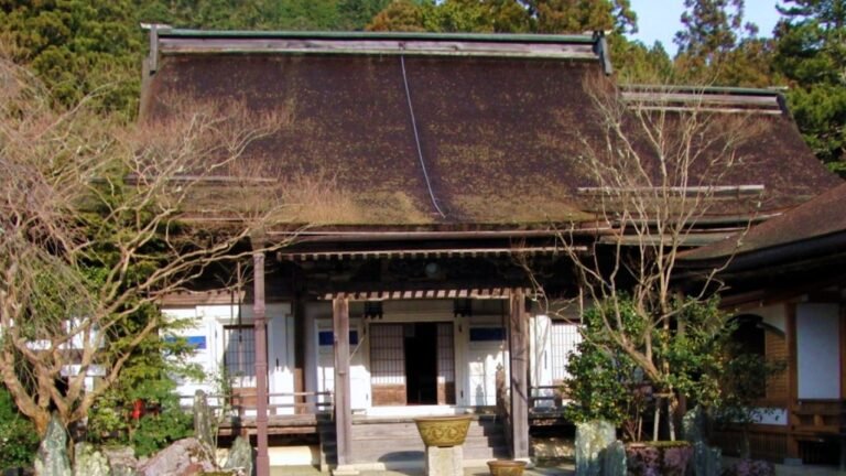 高野山にある茅葺き屋根の宿坊の建物。木製の引き戸、石灯籠、葉を落とした木々が見える
