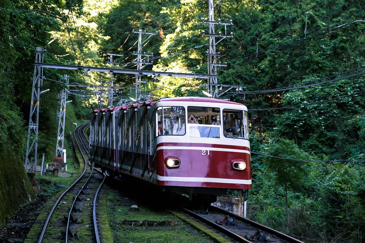 高野山で架線の下、森に囲まれた線路を走る赤と白の南海ケーブルカー