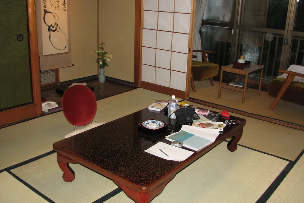 障子のある旅館の部屋で、畳の上に置かれた低い漆塗りのテーブルと赤い椅子