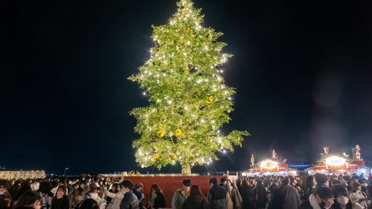 A large illuminated Christmas tree decorated with lights and ornaments above a crowd at a nighttime market in Yokohama