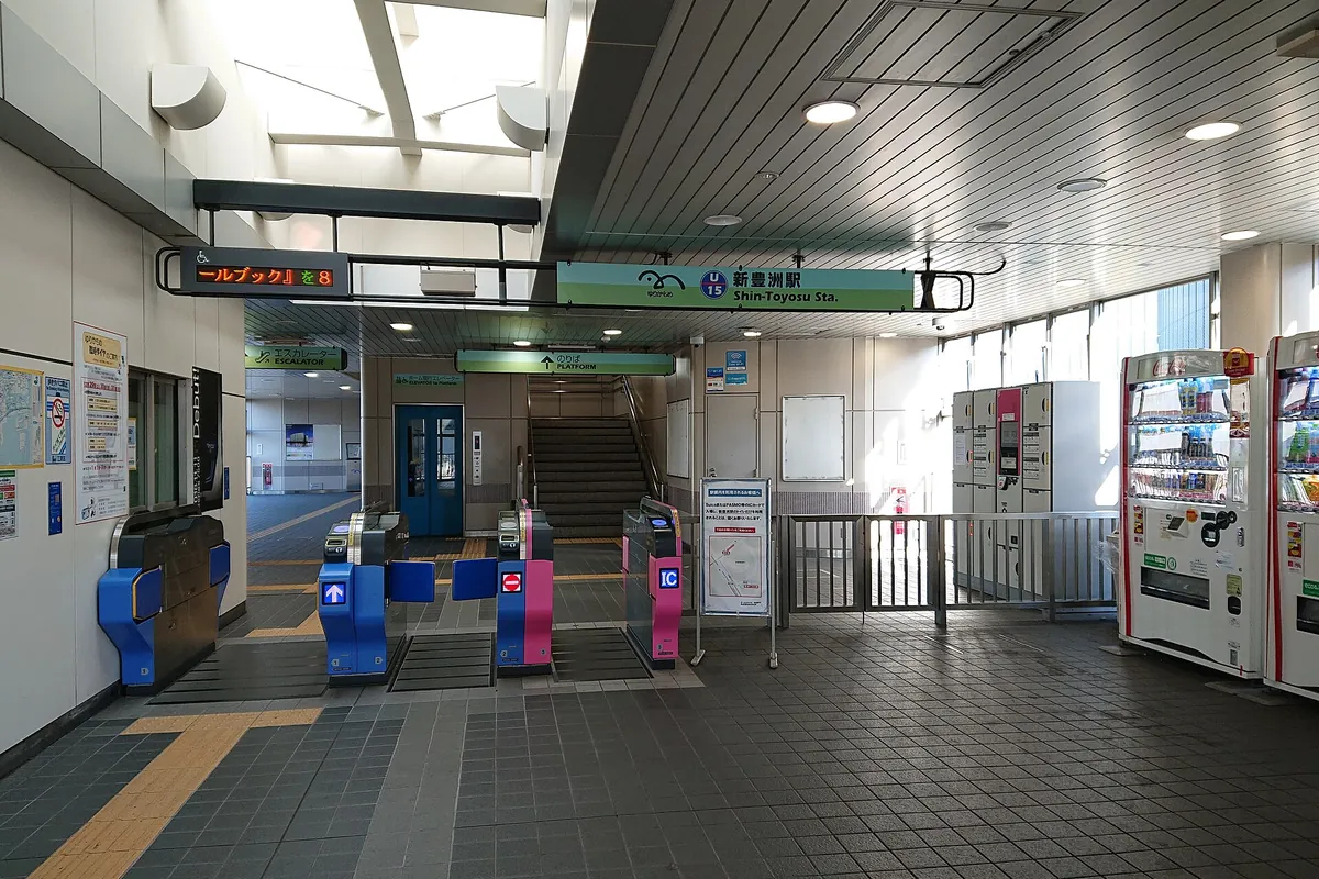 Ticket gates and overhead signage reading Shin-Toyosu Sta. inside a Tokyo train station, with vending machines nearby