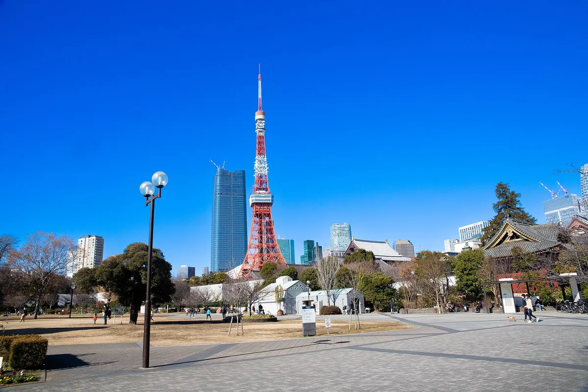 Tokyo Tower rising above trees and buildings beyond a paved plaza with a lamppost in Shiba Park