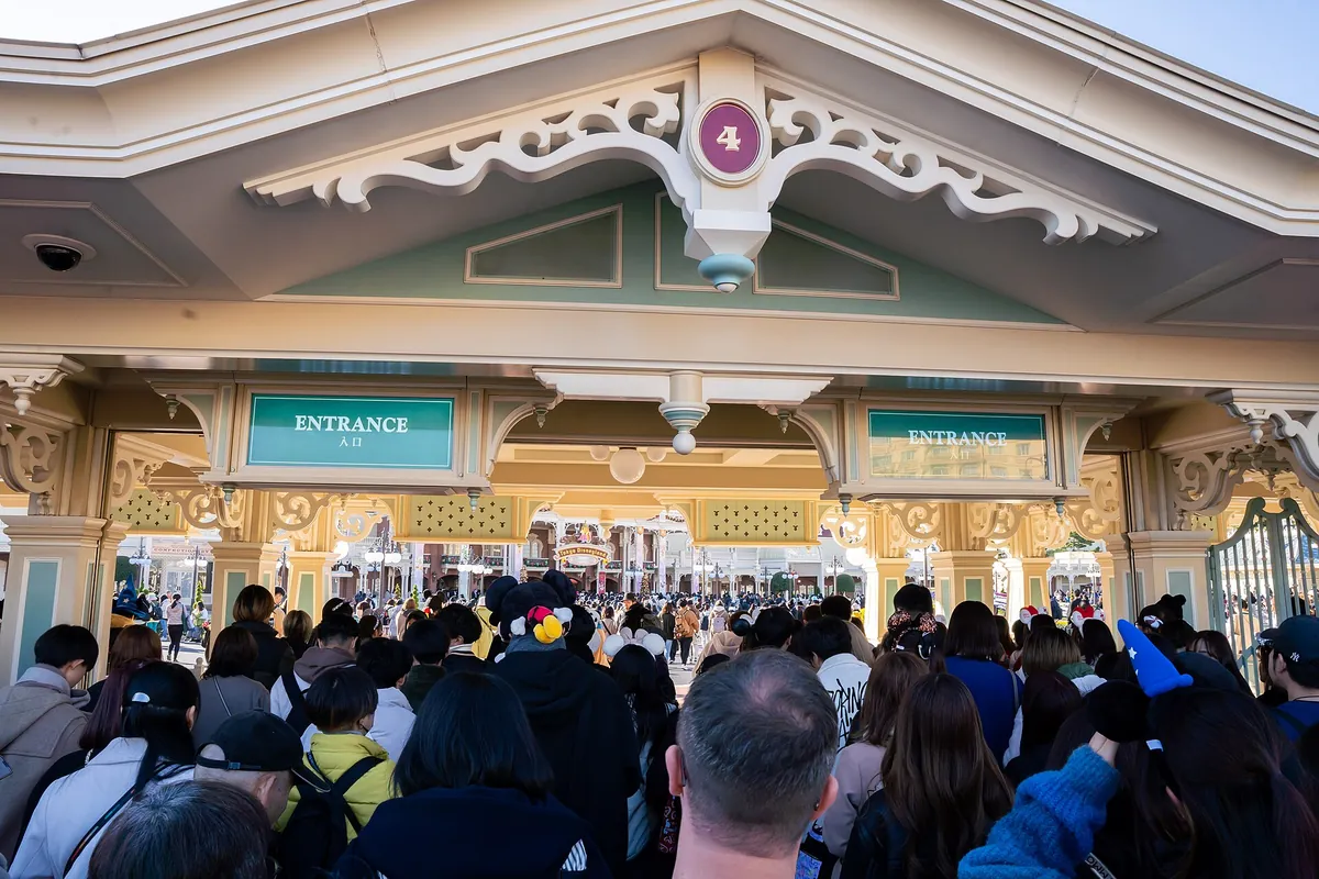 Crowd of guests walking through the Tokyo Disneyland Main Entrance gate marked ENTRANCE and number 4