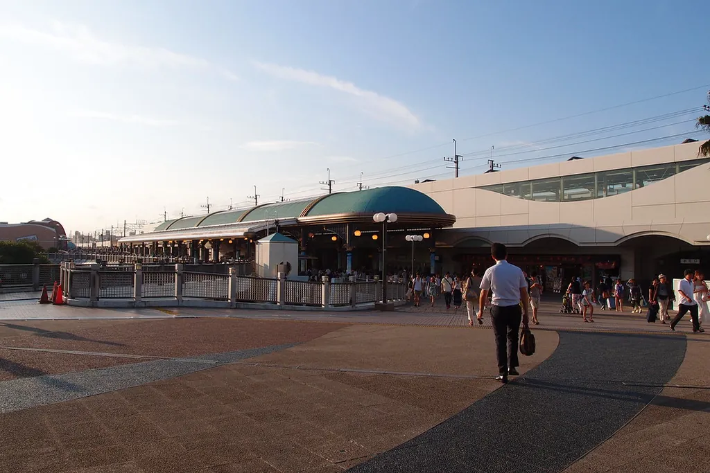 Exterior of JR Maihama Station with its curved green roof, the train station serving Tokyo Disney Resort, with people walking