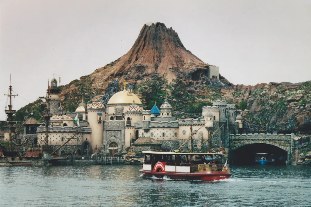 Mount Prometheus rising behind Mediterranean-style buildings at the harbor in Tokyo DisneySea, with a boat on the water