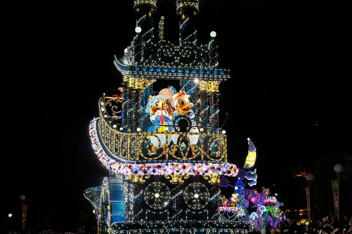 화려한 조명으로 장식된 구조물 위에 도널드 덕과 데이지 덕 인형이 있는 야간 퍼레이드 플로트