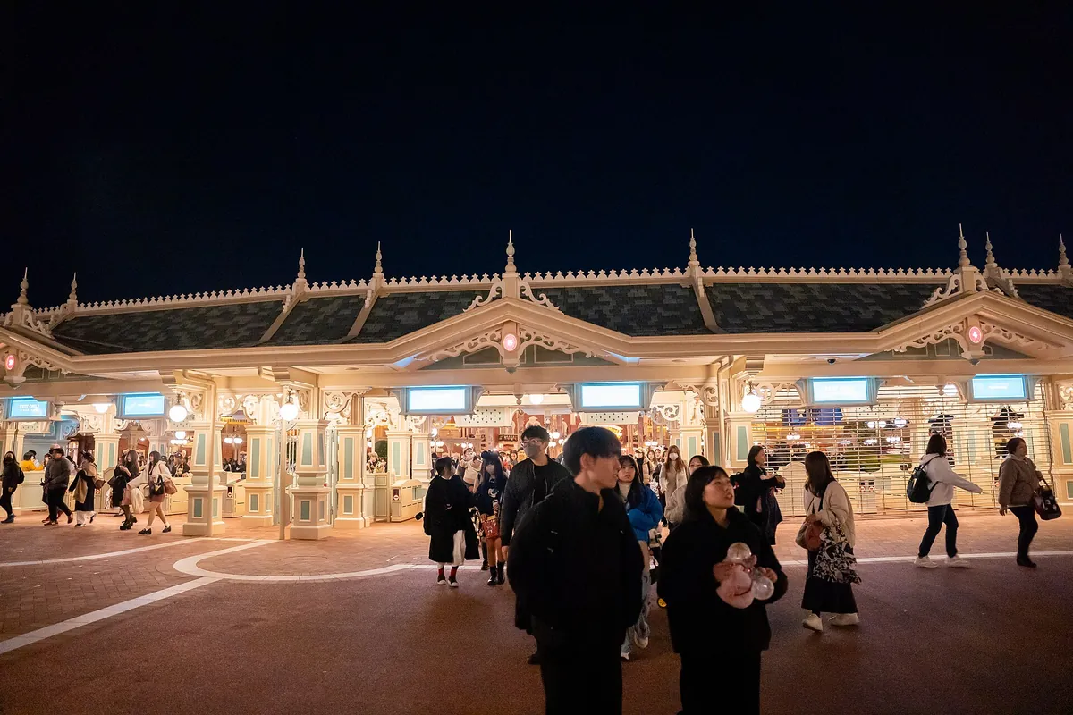 夕方、東京ディズニーランドの装飾された入口ゲートを通るゲストたち