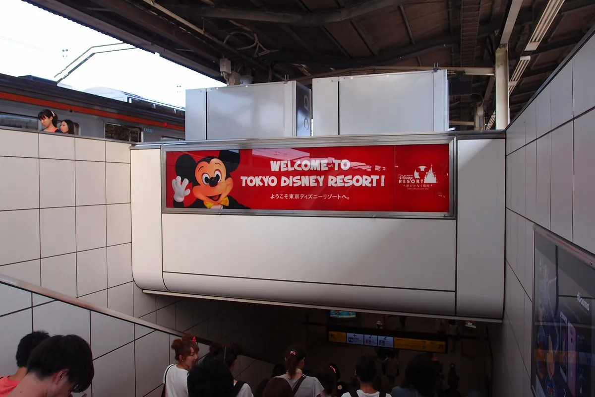 「Welcome to Tokyo Disney Resort」の看板があるJR舞浜駅の通路と、そこを通る人たち