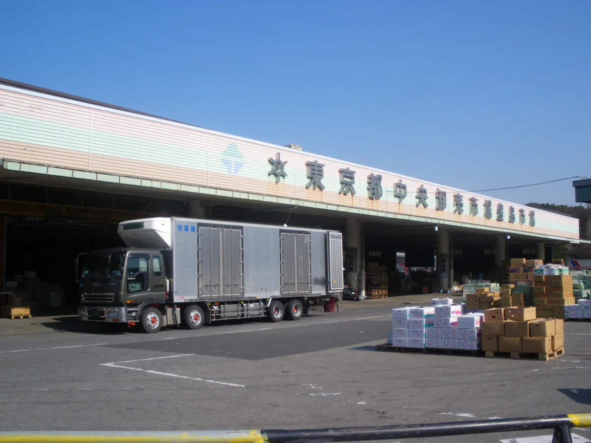 東京都中央卸売市場豊島市場。市場の建物の前にトラックと青果の箱が並ぶ