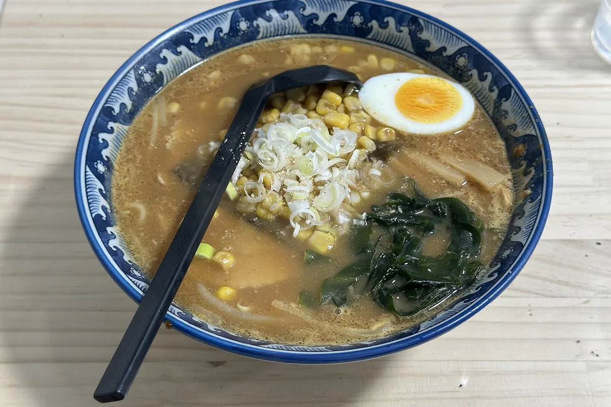 A bowl of Sapporo miso ramen topped with corn, julienned vegetables, a soft-boiled egg, and wakame seaweed