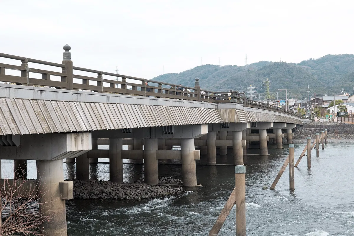 背後に木々の茂る丘が見える、宇治川に架かる長いコンクリートの橋(京都府宇治市)