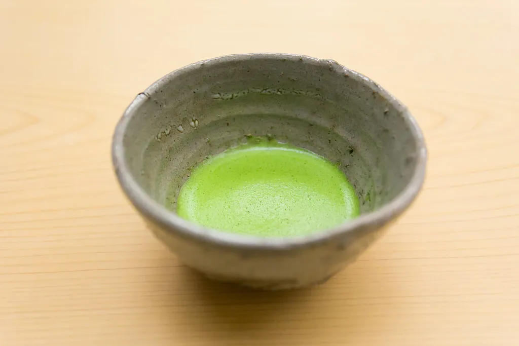 素朴な灰色の陶器の茶碗に、泡立てた抹茶が入っている様子(木のテーブルの上)
