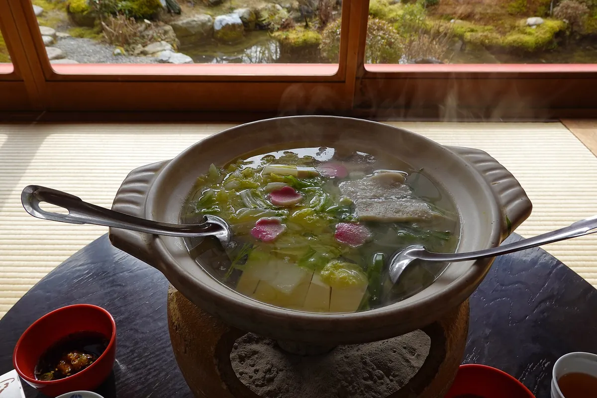 A donabe pot of yudofu with large tofu blocks, mizuna and edible flowers simmering in hot broth
